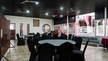 A conference room with round tables and chairs, a wooden floor, and a stage area with curtains.