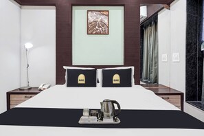 Habitación de hotel con cama, dos almohadas con el logotipo 'OAK', una lámpara de noche, un teléfono, una bandeja con cafetera y tazas, y un cuadro en la pared.