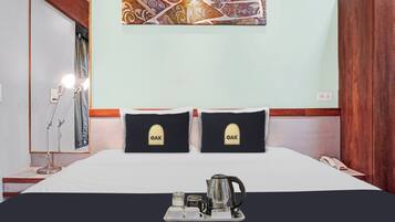 A hotel room with a bed, two pillows with 'OAK' logo, a tray with a kettle, cups, and a small table.