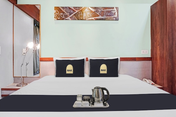 Habitación de hotel con cama, dos almohadas con el logotipo 'OAK', bandeja con tetera, tazas y una mesita.