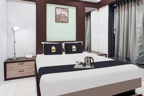 A hotel room with a bed, a bedside table with a lamp, a phone, and a tray with a kettle and cups. - Townhouse OAK Hotel Rajmudra (Pune)