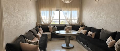 A spacious living room with a large sectional sofa, a round coffee table, and a chandelier.