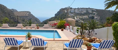 A pool area with lounge chairs and a view of a coastal village.