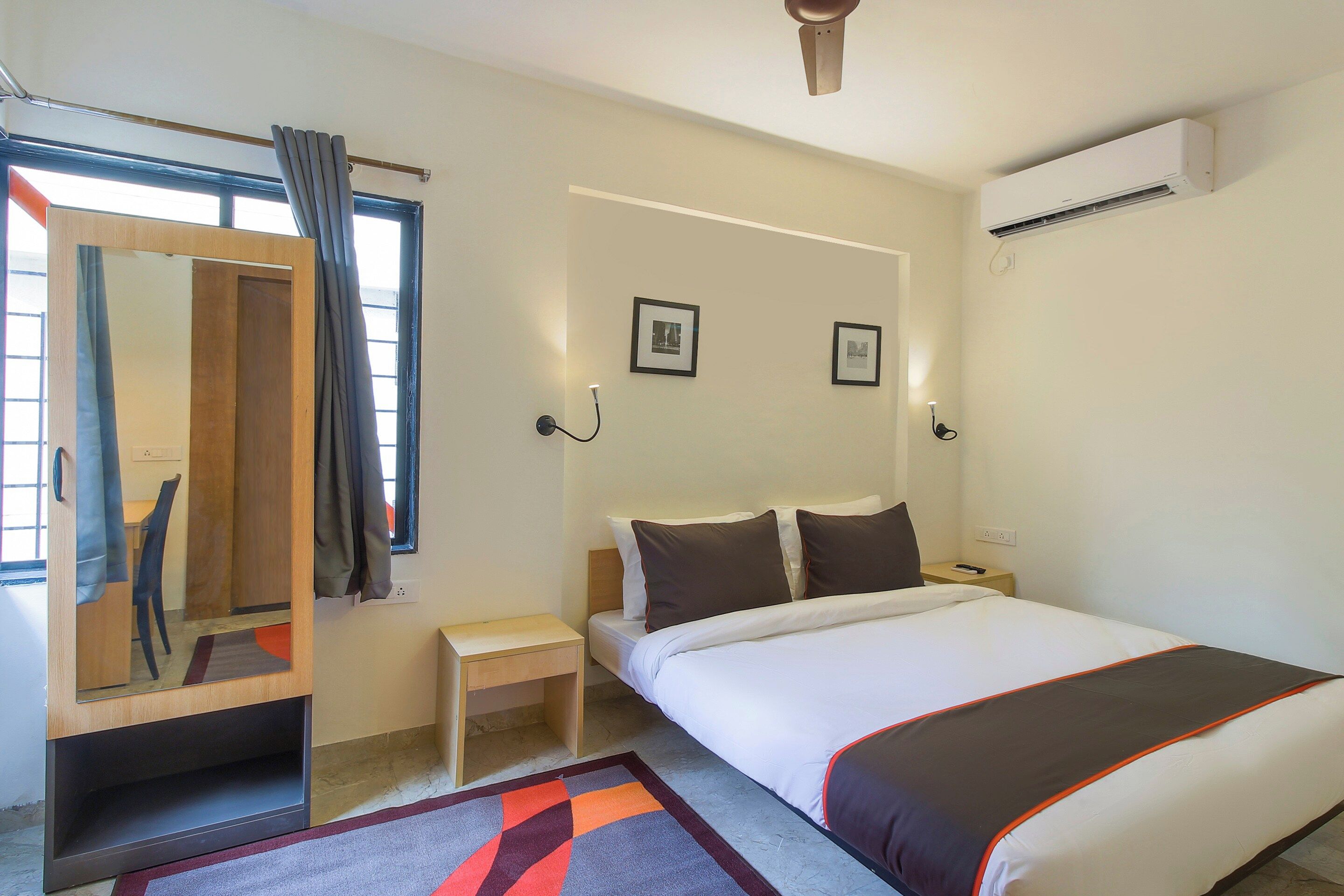 A hotel room with a bed, bedside table, nightstand, and a mirror.