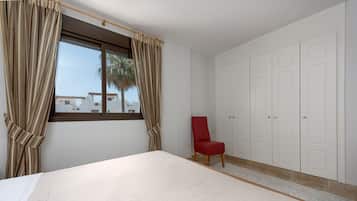 Een slaapkamer met een bed, een rode stoel, een kledingkast en een raam met gordijnen.