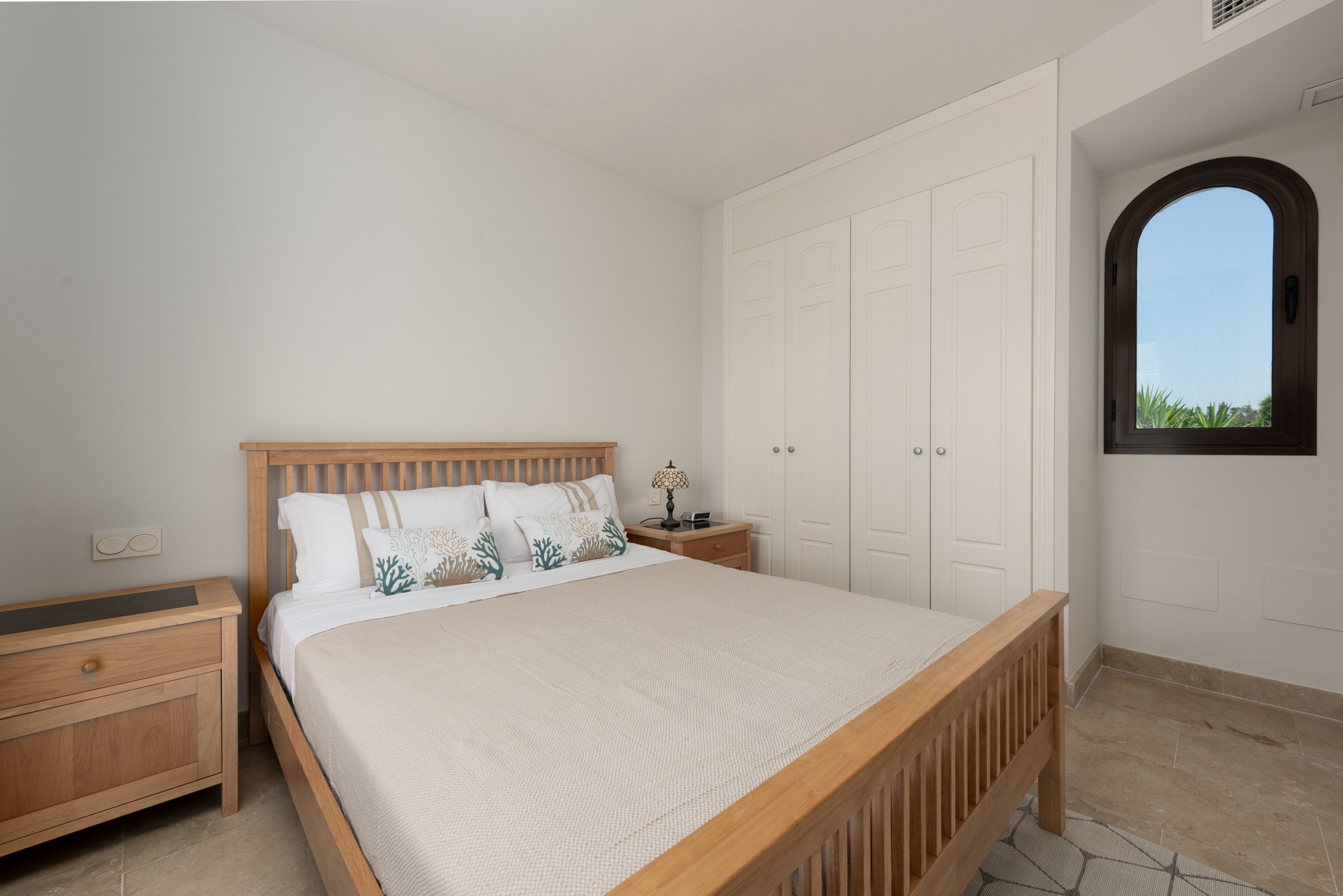 Un dormitorio con una cama de madera, paredes blancas, una mesita de noche, un aparador y un armario.