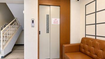 An elevator with a 'LIFT OUT OF SERVICE' sign, a staircase, and a brown leather bench.