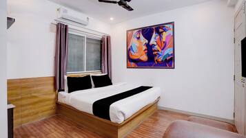 A bedroom with a bed, a ceiling fan, an air conditioning unit, a window with curtains, and a colorful painting on the wall.