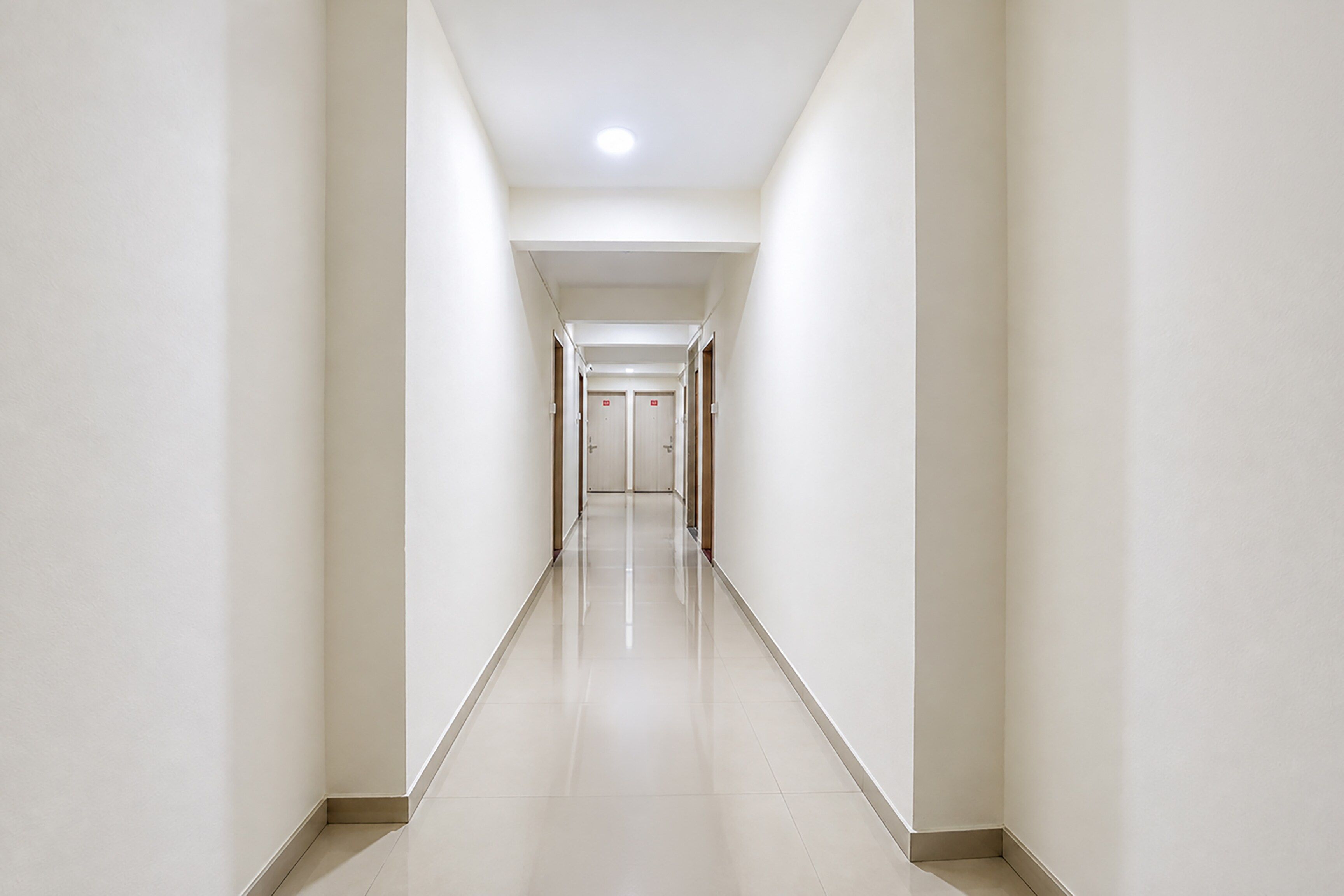 A long, straight hallway with white walls and a shiny floor, leading to a set of doors at the end.
