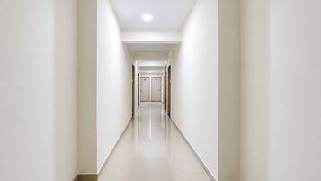A long, straight hallway with white walls and a shiny floor, leading to a set of doors at the end.