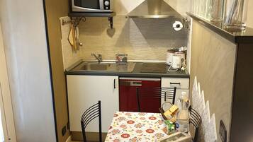 Cocina pequeña con microondas, lavamanos y una mesa con mantel floreado.