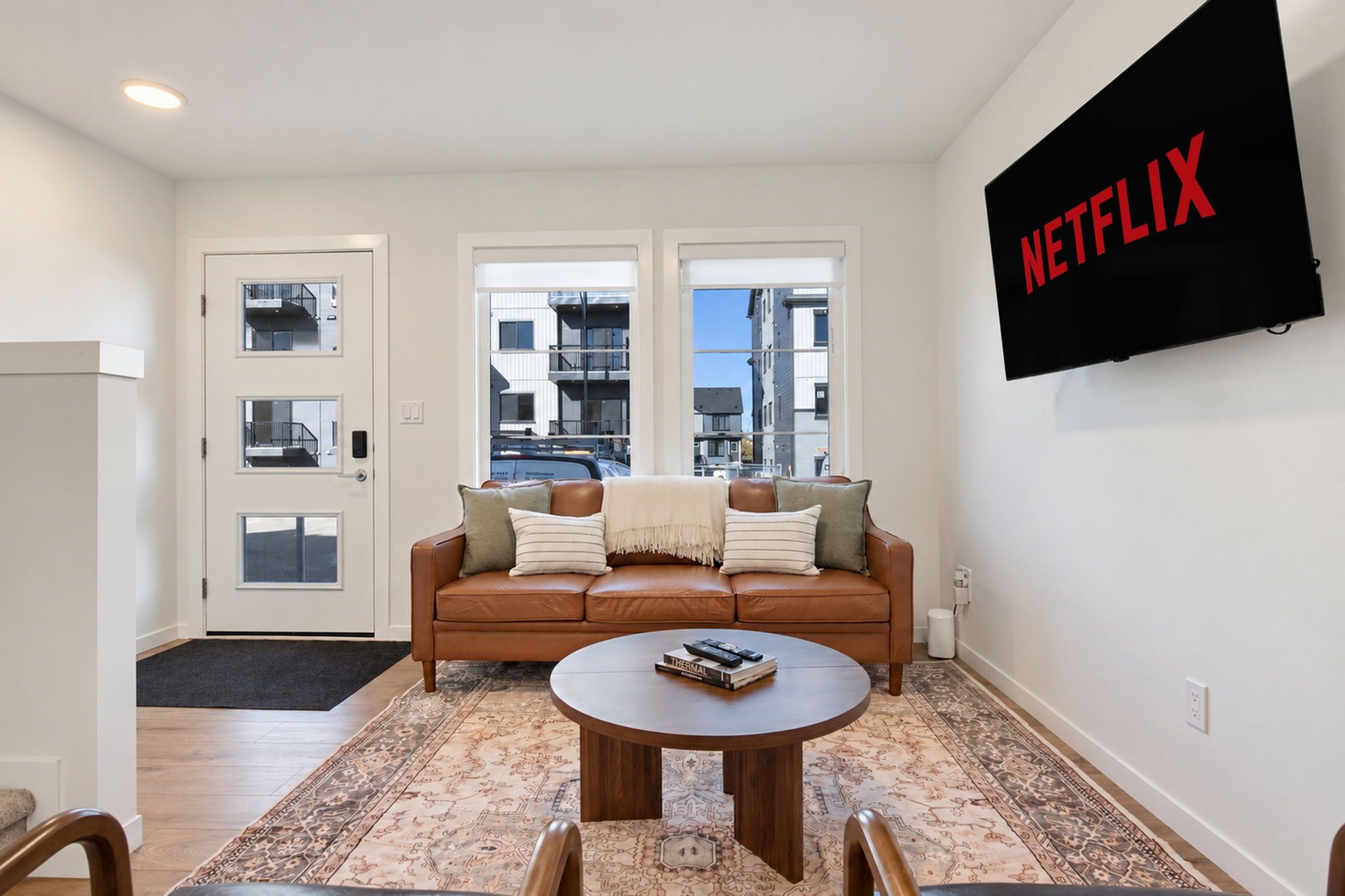 En stue med en brun lædersofa, et sofabord, et mønstret tæppe og et vægmonteret fjernsyn, der viser Netflix-logoet.
