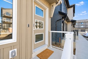 En boligbygning med beige facade, en fordør med et vindue og en lille veranda med dørmåtte.