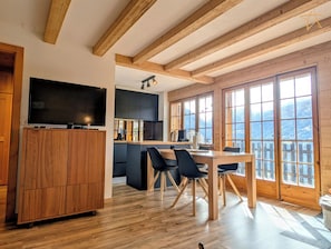 Une cuisine moderne avec des poutres en bois, un coin repas avec des chaises et de grandes fenêtres offrant une vue sur la montagne.
