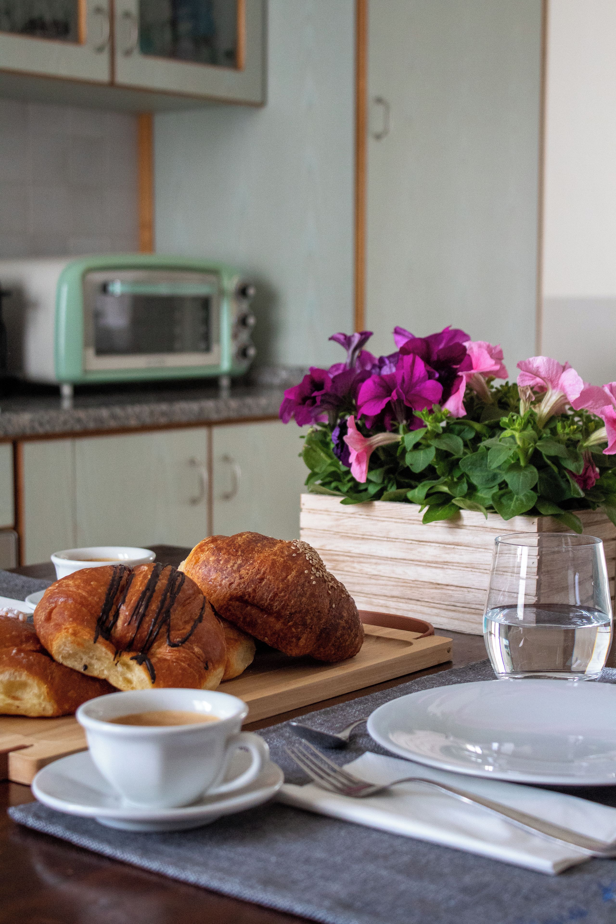 A breakfast setting with pastries, a cup of coffee, and a vase of flowers on a wooden table.