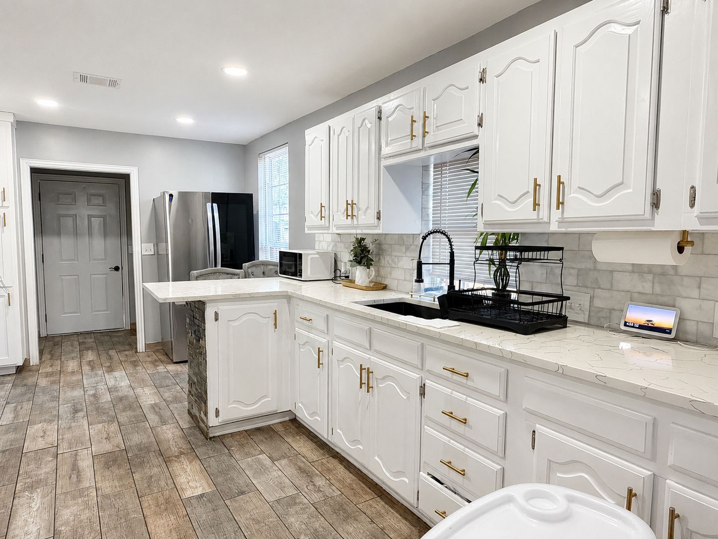 A kitchen with white cabinetry, a stainless steel refrigerator, a microwave, and a sink with a black tray.