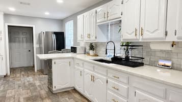 A kitchen with white cabinetry, a stainless steel refrigerator, a microwave, and a sink with a black tray.