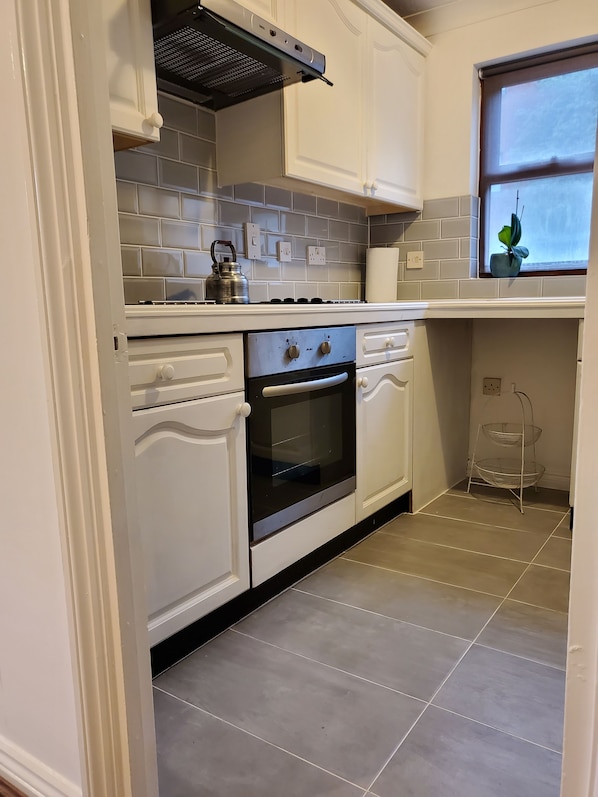 Una cocina con muebles blancos, una estufa a gas y una tetera.