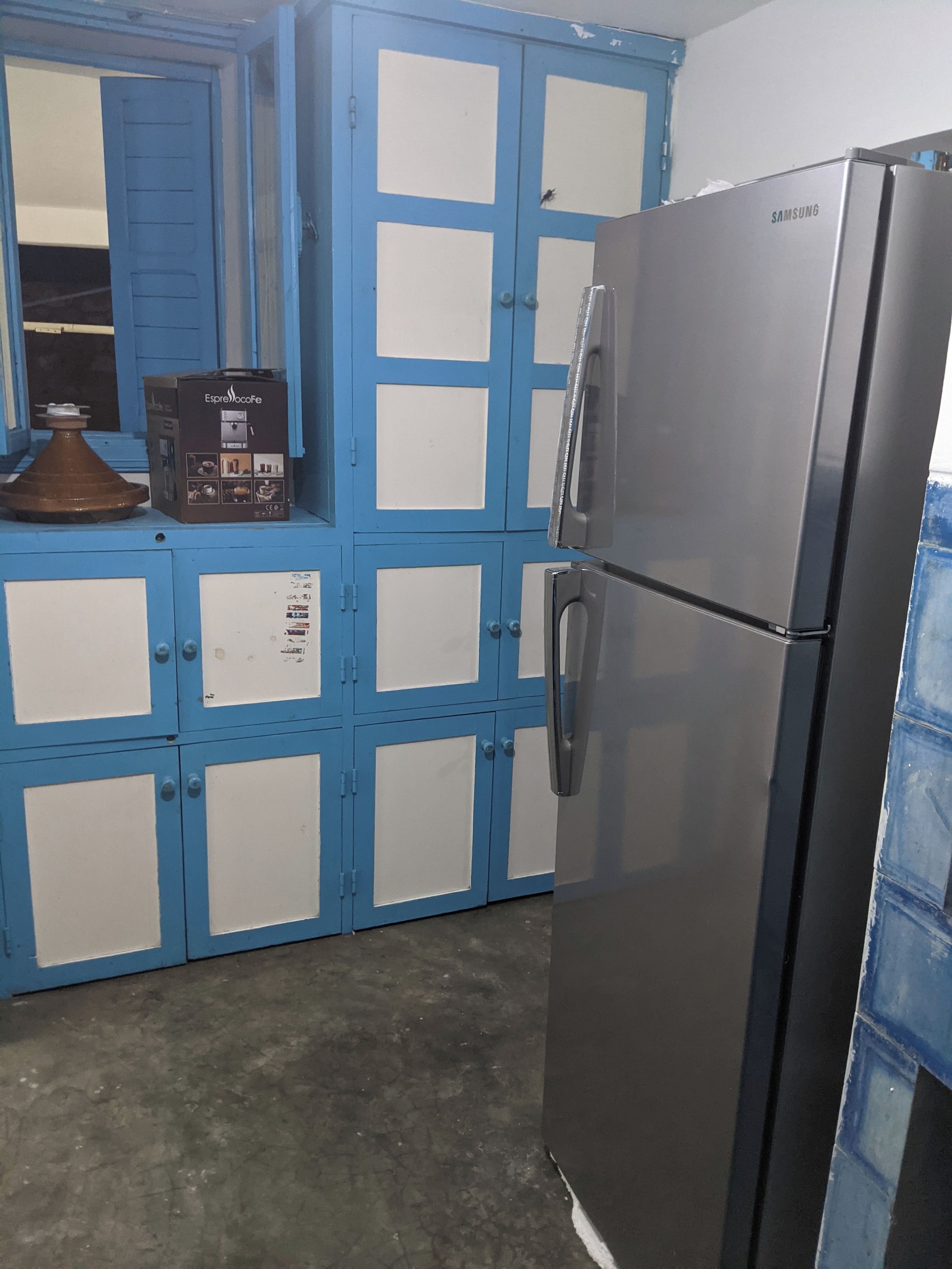 Una cocina con refrigerador de acero inoxidable, armarios azules y un microondas.