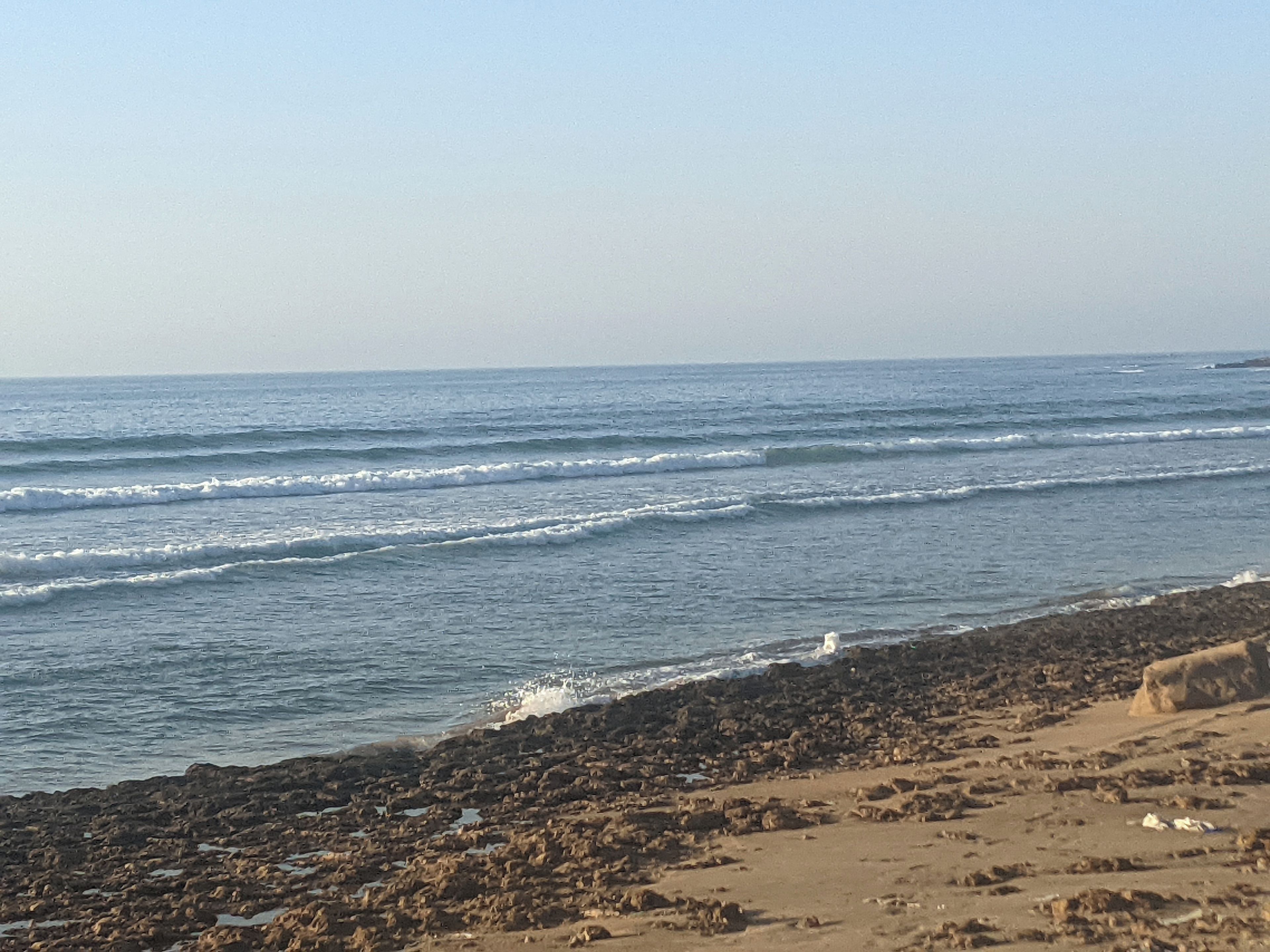 Una playa con olas, costa rocosa y cielo despejado.