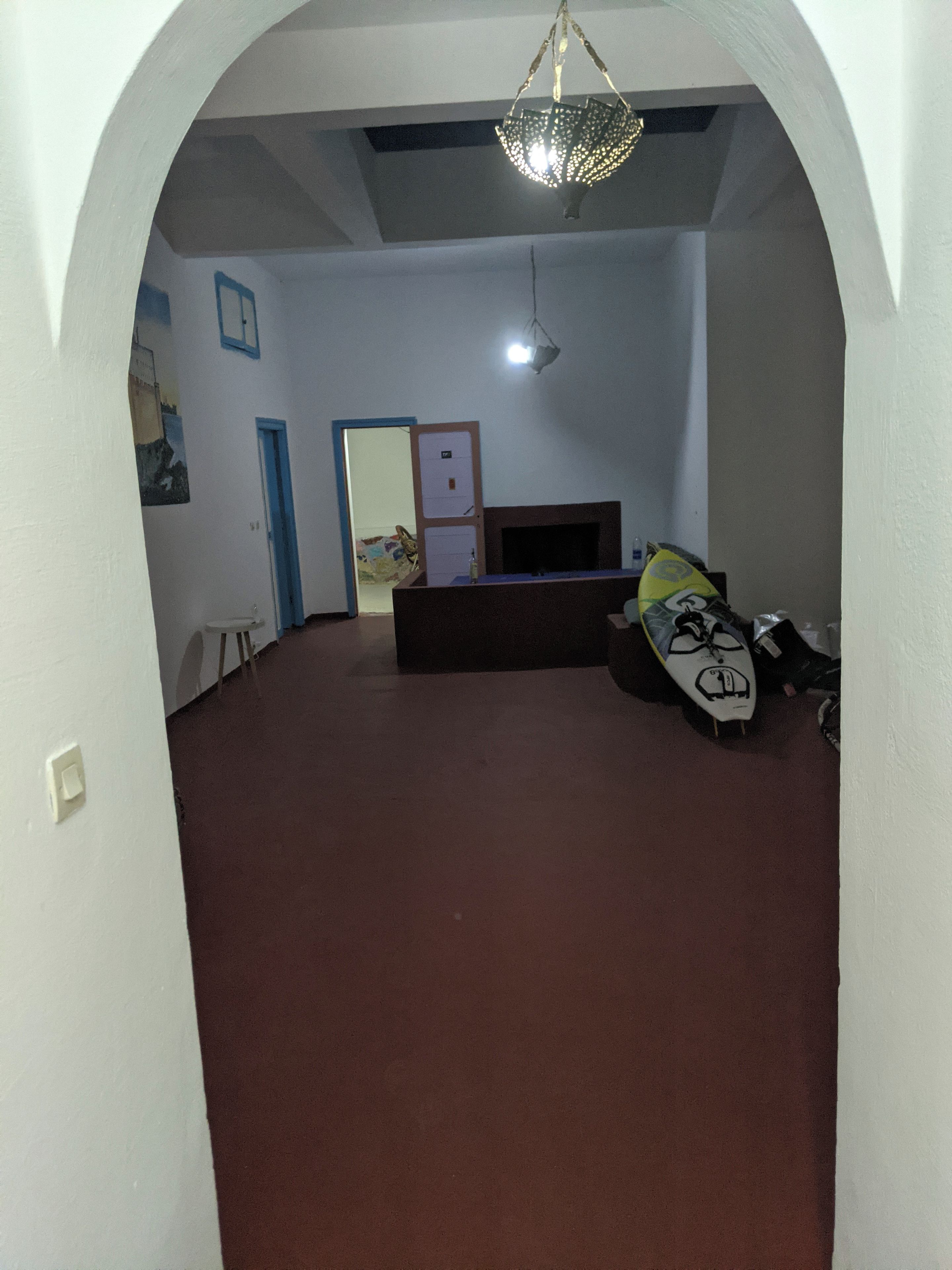 Una habitación con alfombra marrón, pared blanca, puerta, televisor de pantalla plana y lámpara en el techo.