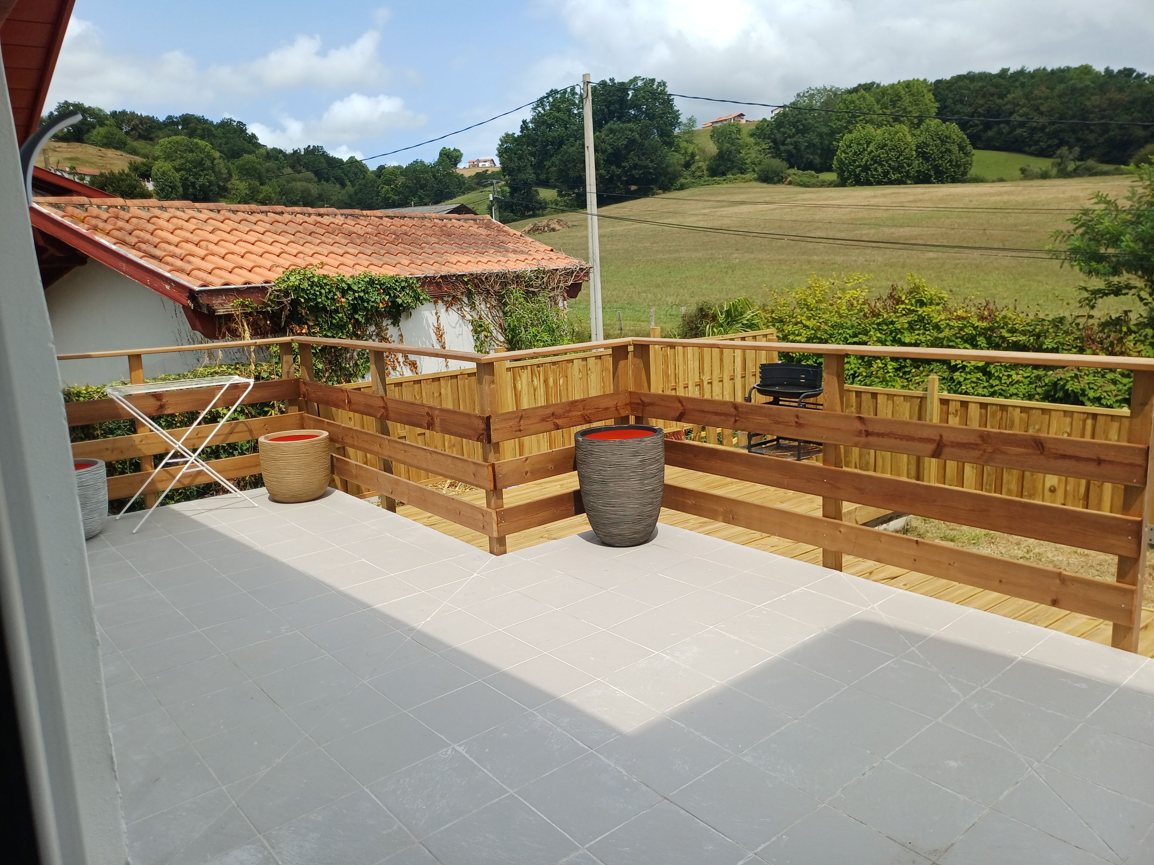 Un balcon doté d’un sol carrelé, d’une barrière en bois et offrant une vue sur un paysage verdoyant.