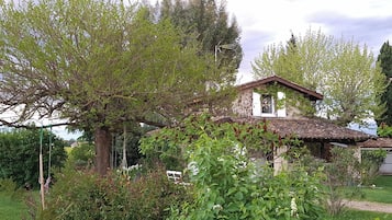 Een landelijk huis met pannendak, omgeven door weelderige begroeiing en bomen.