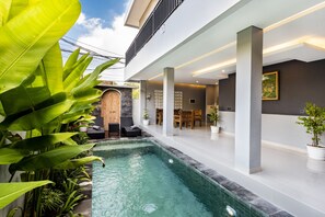 Un área de piscina interior moderna con vistas despejadas al cielo, rodeada de abundante vegetación y un muro de piedra.