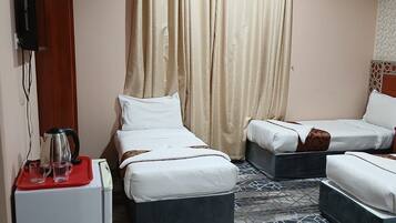Een hotelkamer met twee bedden, een tafeltje met een waterkoker en glazen, en een aan de muur bevestigde televisie.