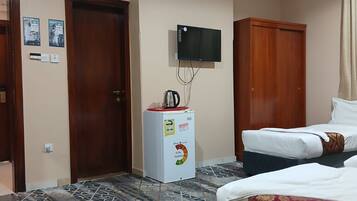A hotel room with two beds, a television mounted on the wall, a minibar, and a patterned floor.