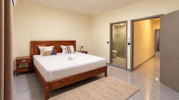 Een moderne hotelkamer met een houten bed, een nachtkastje, een badkamer zichtbaar achter een glazen deur, en een inbouwkoelkast.