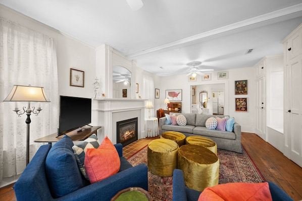 A living room with a fireplace, a sofa set, a television, and a decorative lamp. - Elk Street Cottage - Walk Downtown + Parking (Eureka Springs)