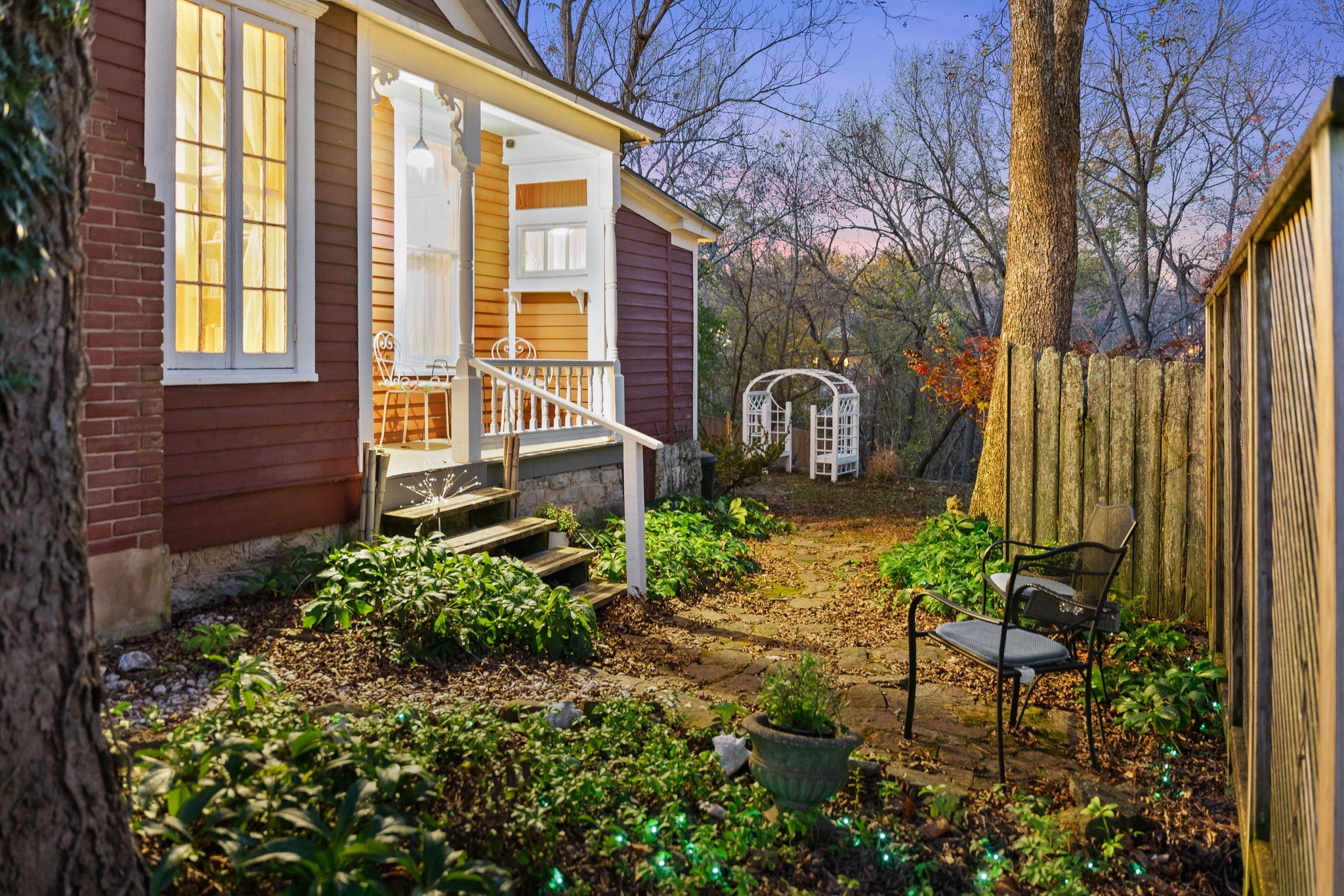 Une maison avec un porche, un jardin avec des plantes et un banc, et une clôture en bois.