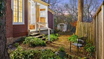 Une maison avec un porche, un jardin avec des plantes et un banc, et une clôture en bois.