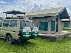 A safari vehicle parked next to a tented accommodation with a clear sky.