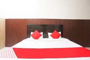 Habitación de hotel con cabecera de madera, ropa de cama blanca y dos almohadas rojas.