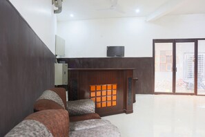 A room with a sofa, a television on a stand, and a sliding glass door leading outside. - Hotel O Mayur Hotel (Faridabad)