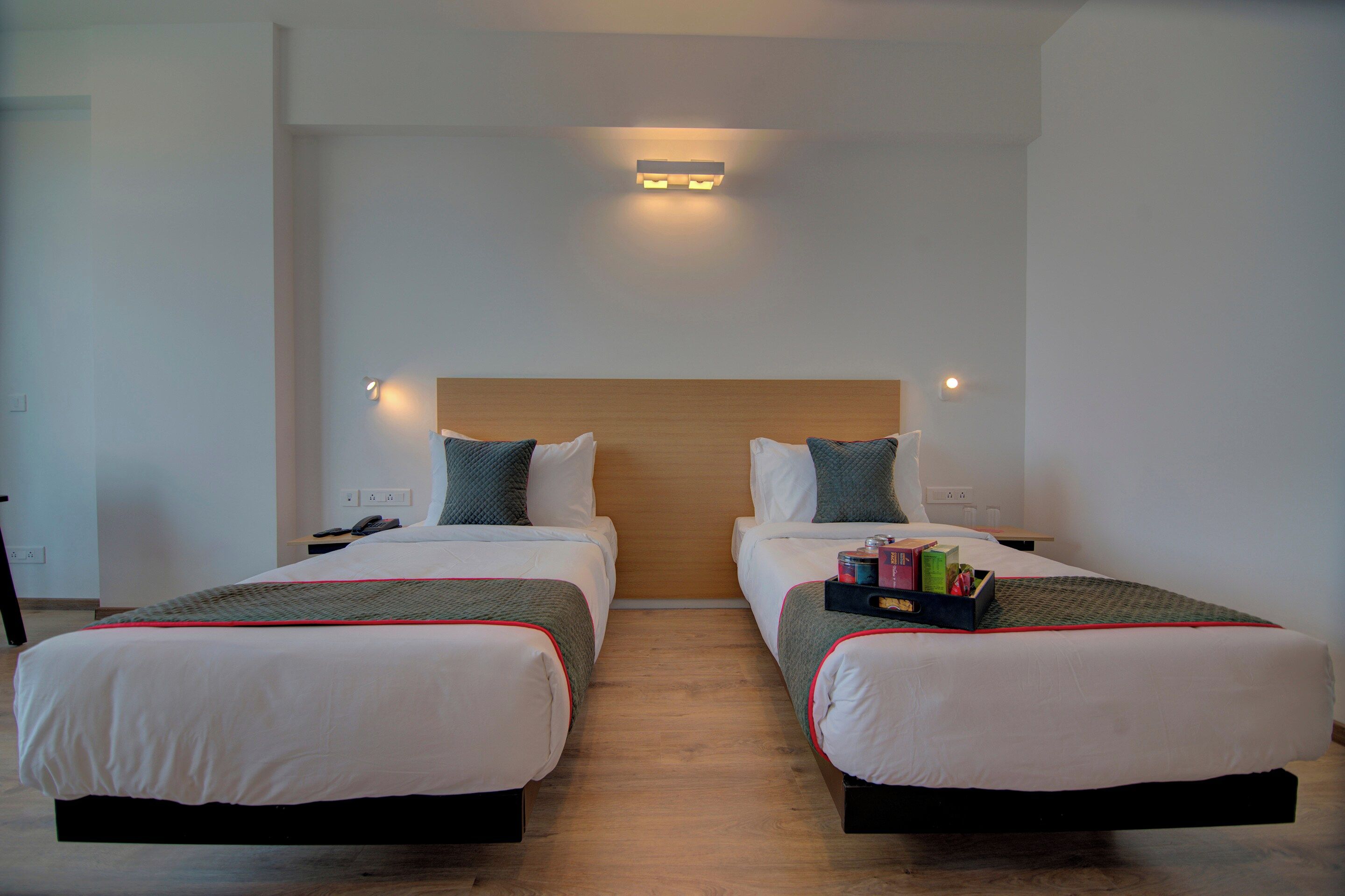 A hotel room with two beds, a wooden headboard, bedside lamps, and a bedside table with a phone and remote control.