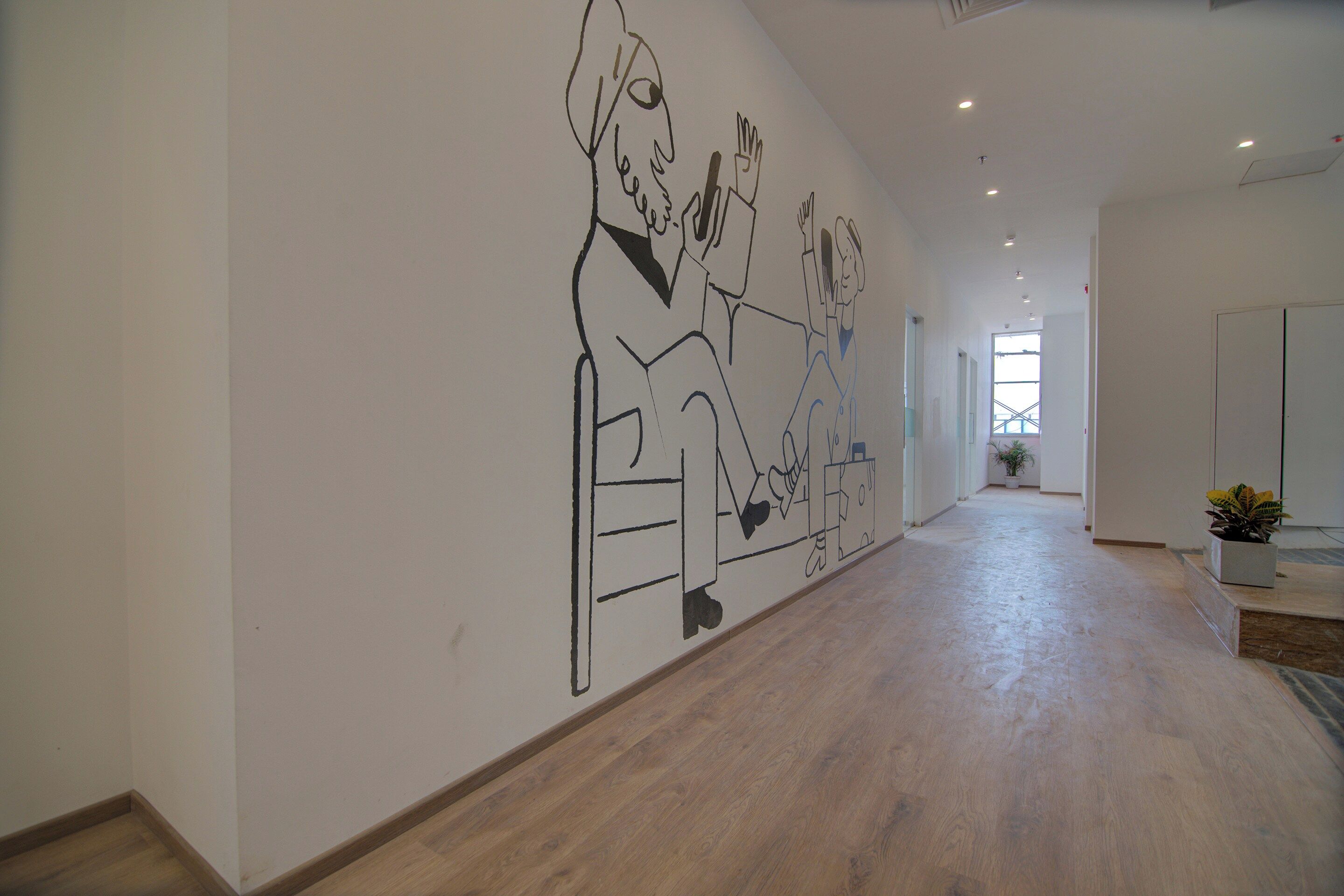 Un pasillo amplio con techo alto, piso de madera y un gran mural en la pared.