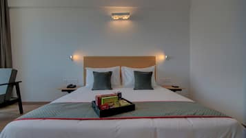 A hotel room with a bed, bedside tables, a chair, and a tray with snacks.