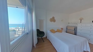 Un dormitorio con cama, una silla, un aparador y vista al mar.