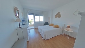 Un dormitorio con cama, mesita de noche, lámpara, ventilador y vistas al exterior.
