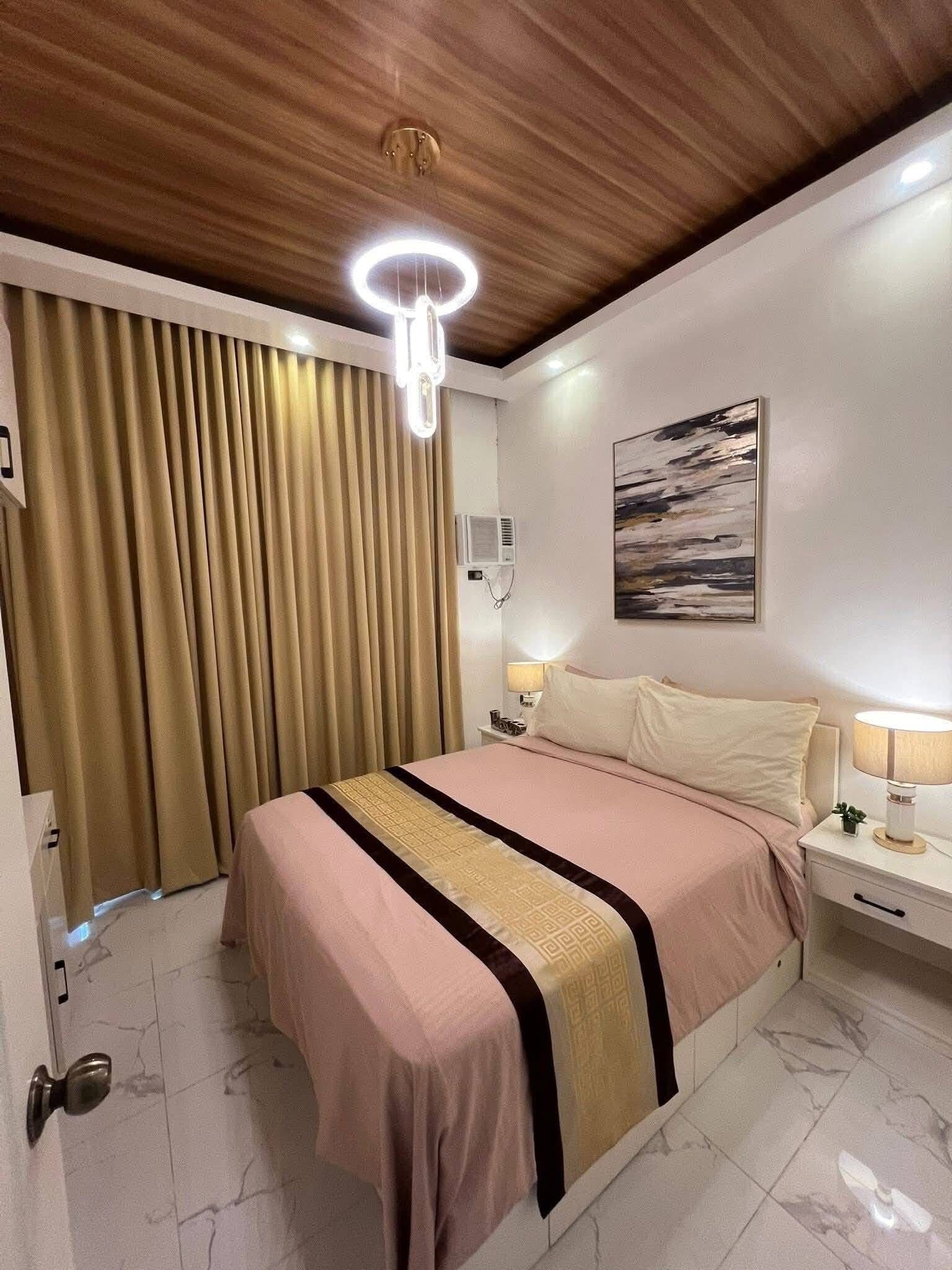 Habitación de hotel con cama, mesitas de noche, lámpara, un cuadro y una lámpara en el techo.