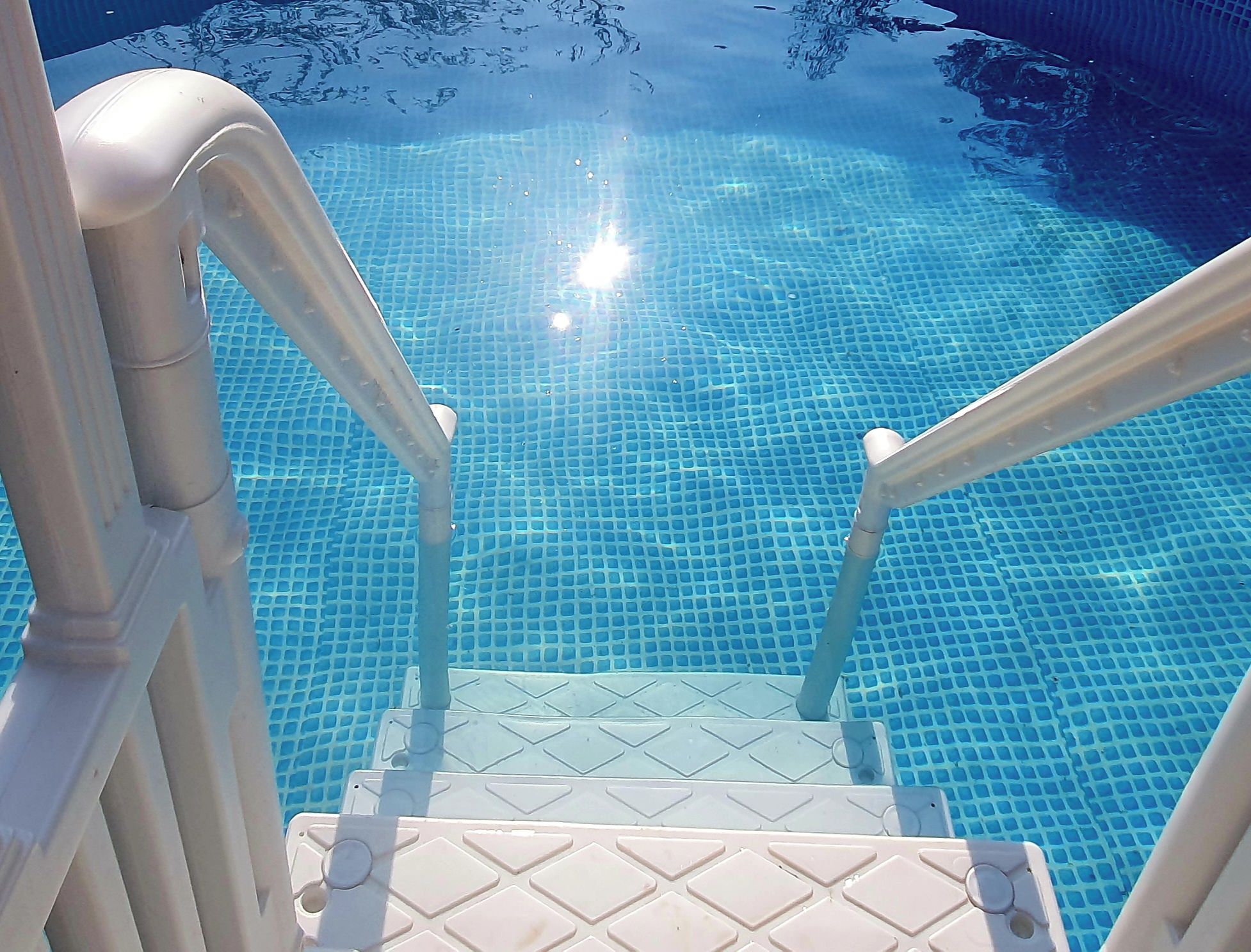 A clear blue pool with a tiled floor and a set of stairs leading into the water.