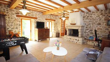 A cozy living room with a stone wall, wooden beams, a fireplace, a television, and a foosball table.