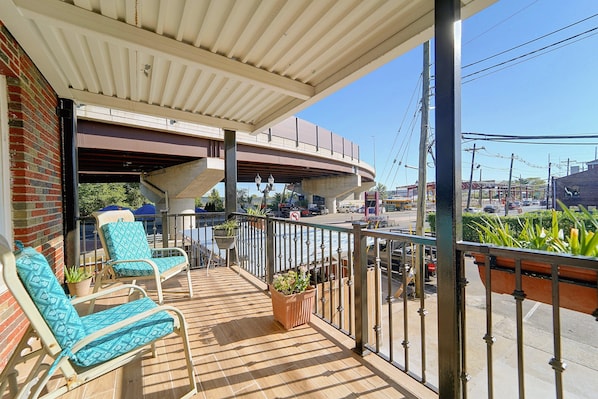 A balcony with two lounge chairs, a potted plant, and a view of a street with vehicles and a bridge.