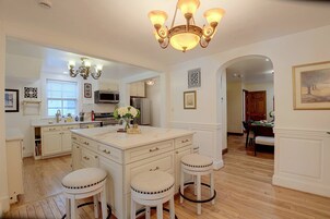 A kitchen with white cabinetry, a central island with stools, a chandelier, and a dining area with a wooden table and chairs.