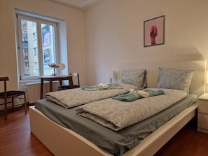 Un dormitorio con una cama, una silla, una mesa y un ventanal.