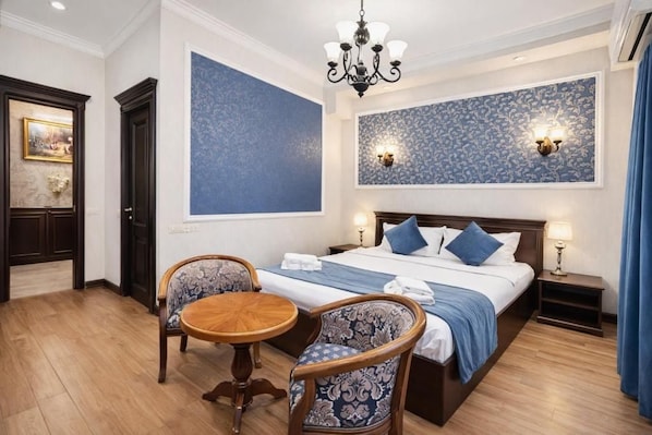 Habitación de hotel con una cama grande, dos sillones, una mesita redonda y un candelabro.