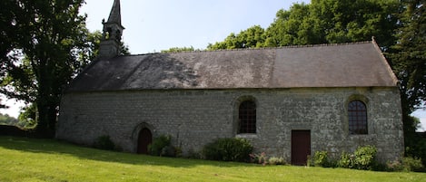 A stone church with a bell tower, arched windows, and a grassy foreground.
